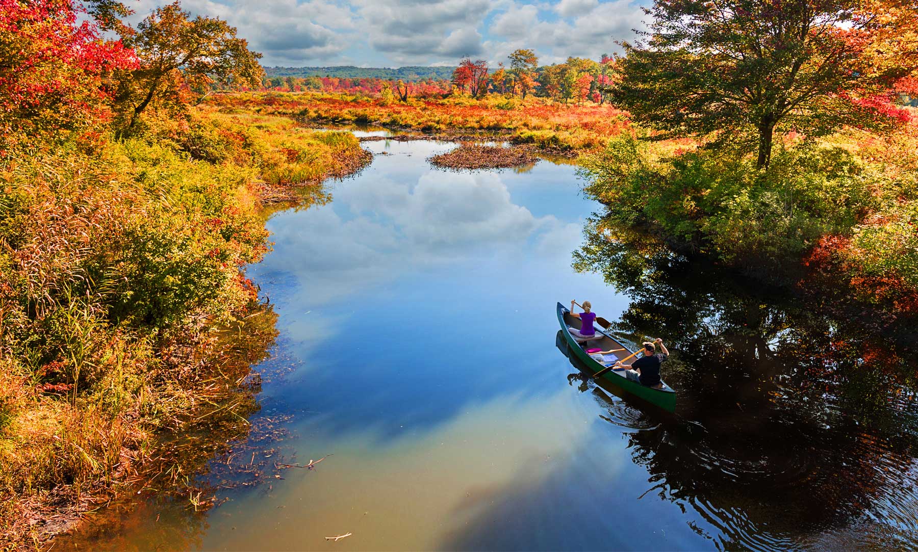 Two people on a canoe, on a river, surrounded by fall foliage