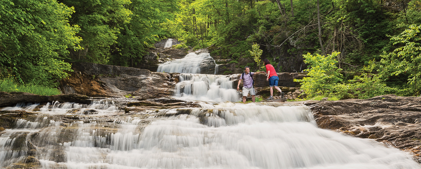 Two people hiking over a river at Kent Falls