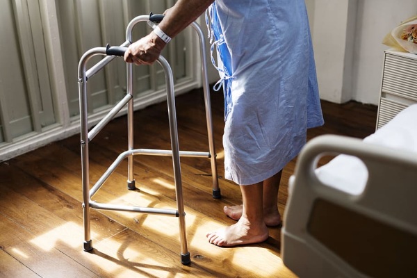 A person wearing a gown, using a walker in a hospital room..