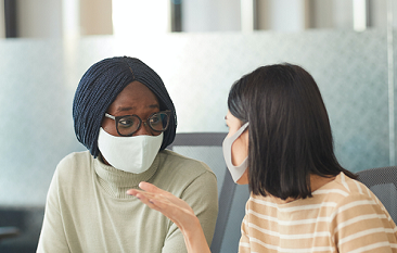 Black and Asian female co-workers  in CT office talk to each other  with COVID-19 masks on