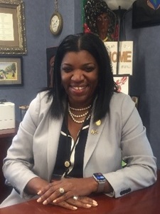 Photo of Commissioner Dorantes smiling at her desk in a grey blazer