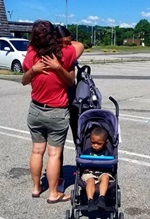 Photo of Becca and Destiny hugging with Jayden in the stroller next to them