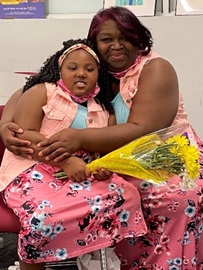Alivia and her grandma hugging on adoption day in matching pink skirts and vests with a blue top