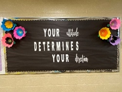 Board with black background and bright flowers that read, "Your attitude determines your direction"