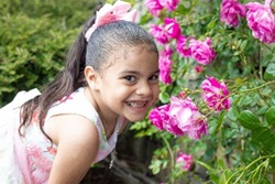 Aynara with a broad smile in front of pink roses