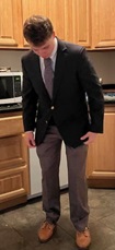 A person in a suit and tie standing in a kitchen Description automatically generated with medium confidence