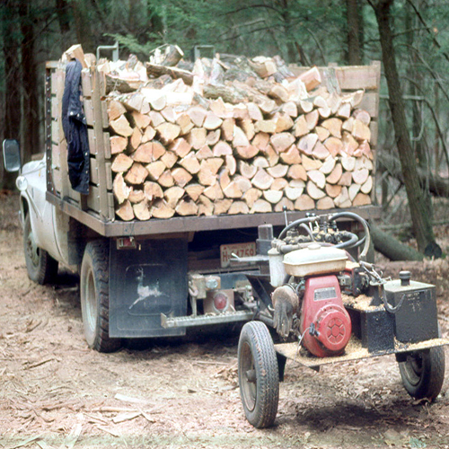 A truck with its bed filled with split firewood and towing a wood splitter.