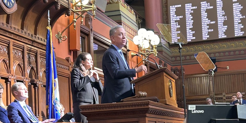 Governor Ned Lamont speaking from the dais in the Hall of the House of Representatives.