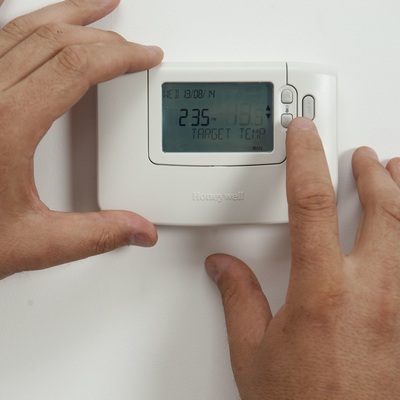 Two hands adjusting the temperature on a home thermostat.