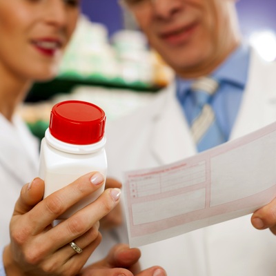 Two pharmacists in white lab coats holding a bottle of medication and a paper prescription.