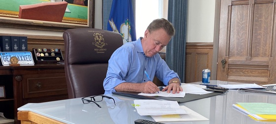Governor Lamont sitting at desk and signing legislation