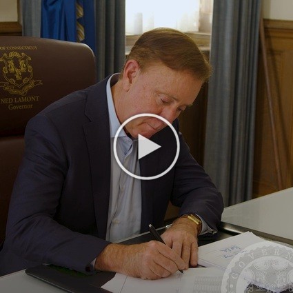 Video of Governor Lamont sitting at a desk and signing a bill