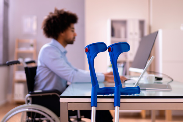 Man at computer in wheelchair with crutches