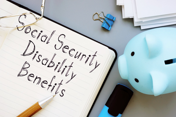 The text social security disability benefits is handwritten in a notebook with piggy bank