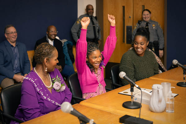 young girl smiles and raises her hands in excitement during her court hearing for adoption