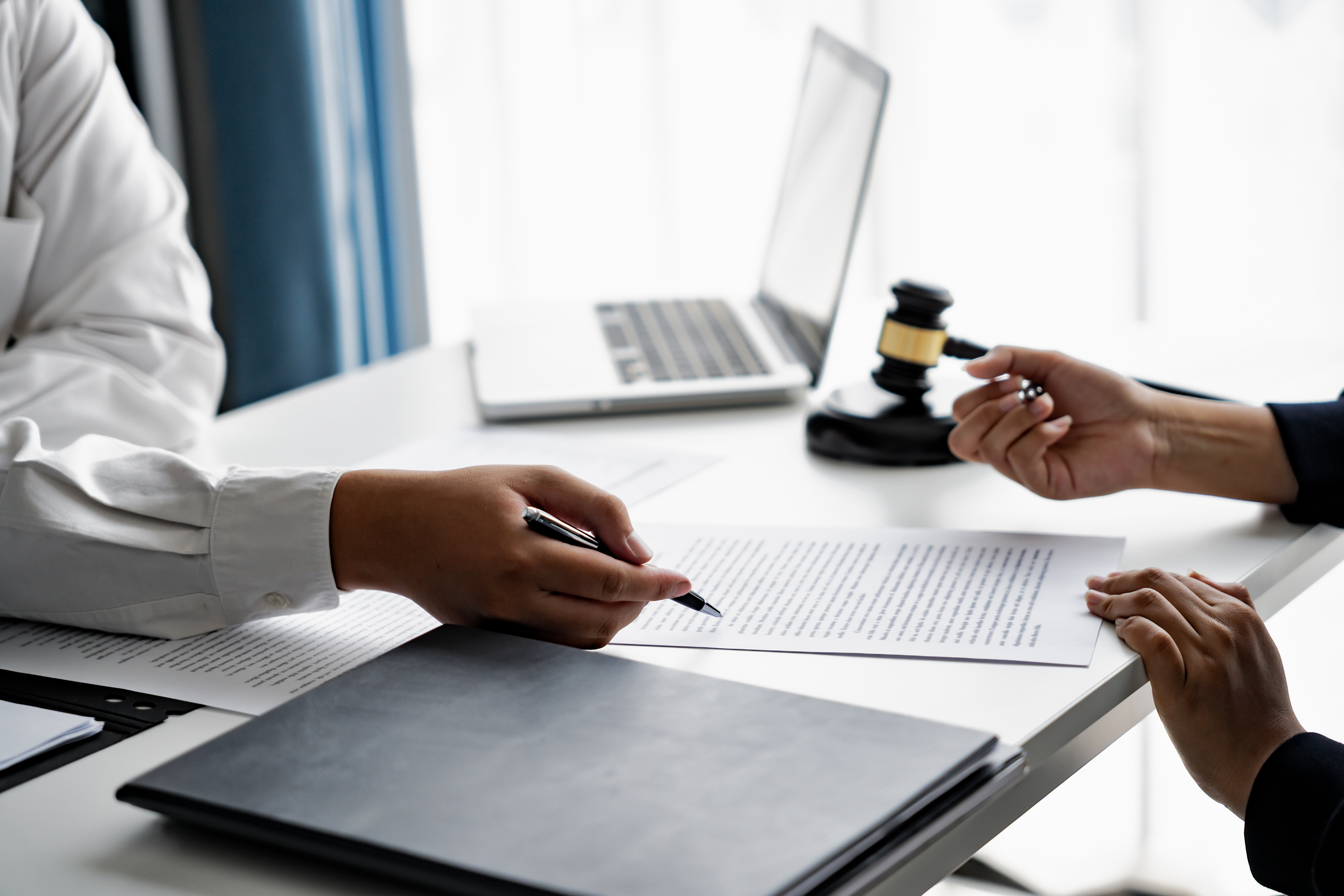 two people's hands mark up a legal document next to a laptop and gavel