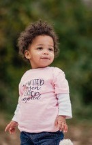 Photo of baby Amari standing on her own, looking into the distance in a pink shirt