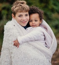 Photo of one of the Baxter sons holding Amari, both wrapped in a fluffy white blanket