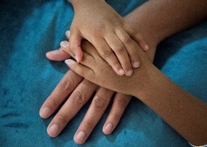 Photo of a child's hands over an adult's on a teal blanket