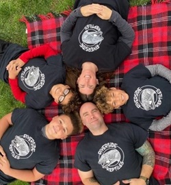 Aerial photo of a family in matching black shirts lying in a circle on a red plaid blanket
