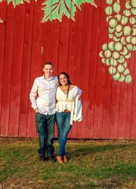 Kally and Zander stand in white shirts and jeans in front of a red barn
