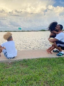 Rodney and his two children at the beach; he is hugging his daughter while his son watches