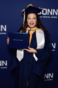 Gabbie in full UCONN commencement regalia with her degree in front of a UCONN background