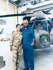 Willie proudly stands with his daughter Shaneria.  She is in her uniform, and the two stand in front of a helicopter.