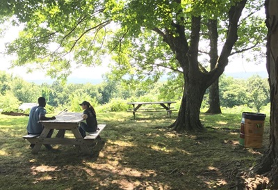 View of the picnic area with a man and woman sitting at one of the picnic tables overlooking the mountain view at Old New-Gate. 