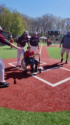 A student in a wheelchair holds a bat at home plate, surrounded by East Lyme baseball players