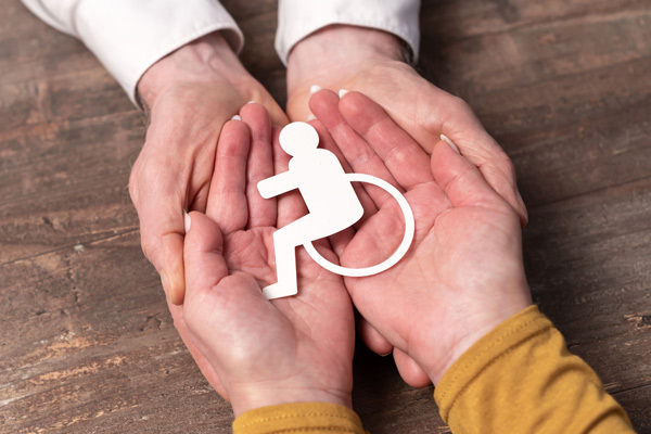 Two person holding a cutout of a disability wheelchair symbol