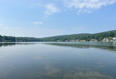 A landscape image of Beseck Lake in Middlefield, CT showing open water with some vegetation, houses and trees on the horizon, and an open blue sky.