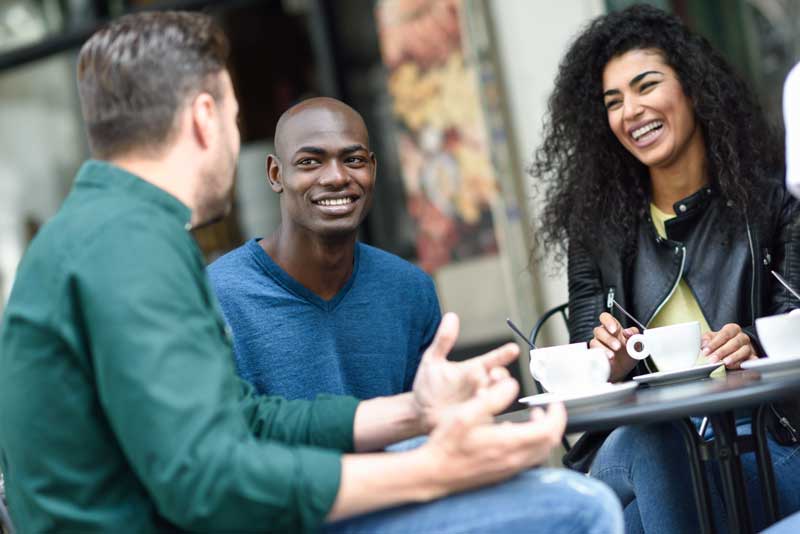 Three people sitting at a cafe table, smiling and laughing over coffee.