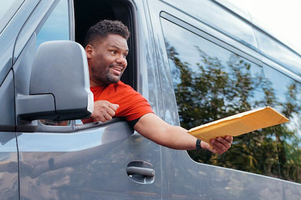 Black man smiles as he delivers a package out the window of his vehicle