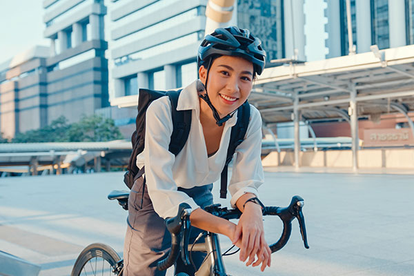 Asian businesswoman going to work at office stand and smiling wear backpack look at camera with bicycle on street around building on a city. Bike commuting, Commute on bike, Business commuter concept