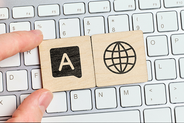 Apple keyboard with two wooden tiles, one with a black painted globe icon and the other with a painted alt text icon being held in place with two fingers..
