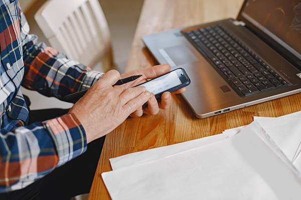 Man with Laptop and Phone taking Notes Writing for Mobile Devices.