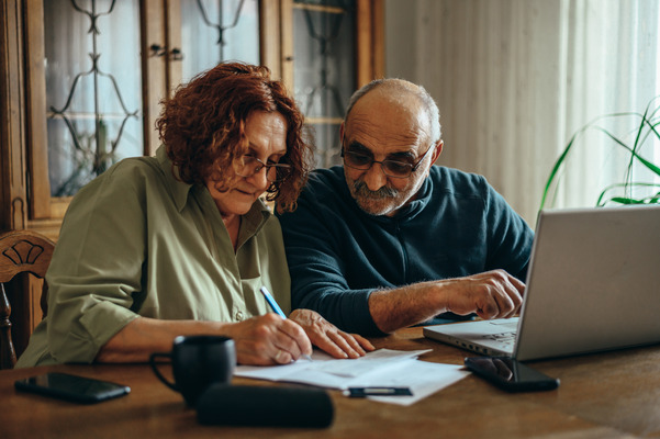 Image of two individuals doing paperwork in front of a laptop, both sitting at at kitchen table