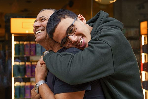 A teen boy leans over to hug his father