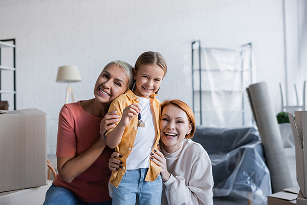 preteen girl holding key near happy same sex parents in new apartment