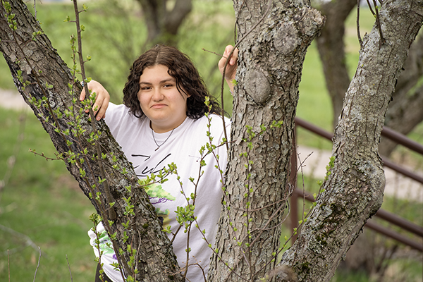 teen girl smiles through budding tree branches
