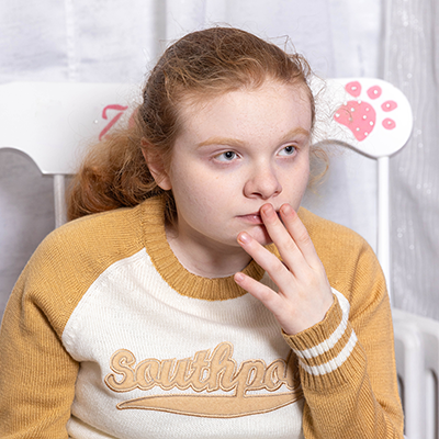 a red headed girl holds her finger to her lips and gazes into the distance