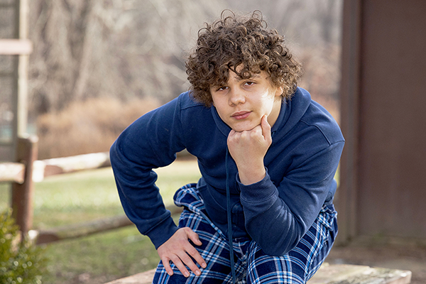a boy with curly brown hair rests his chin on his hand