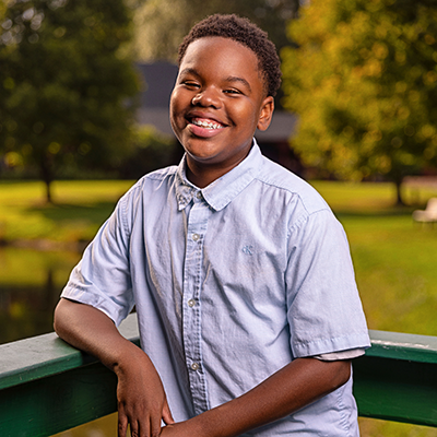 Little black boy in a button up shirt smiles outdoors