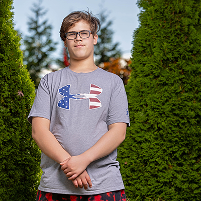 a teenaged boy with glasses smiles outdoors