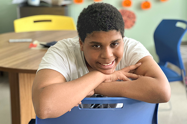 young black boy sits and smiles on a school chair