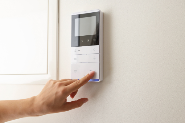 Image of modern thermostat on wall in house, individual is pressing button to indicate turning on heat