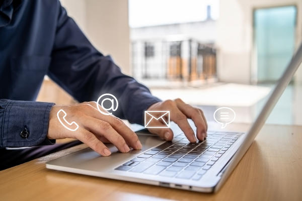 Image of individual typing on computers showing various services including a phone icon, email envelope and a chat feature