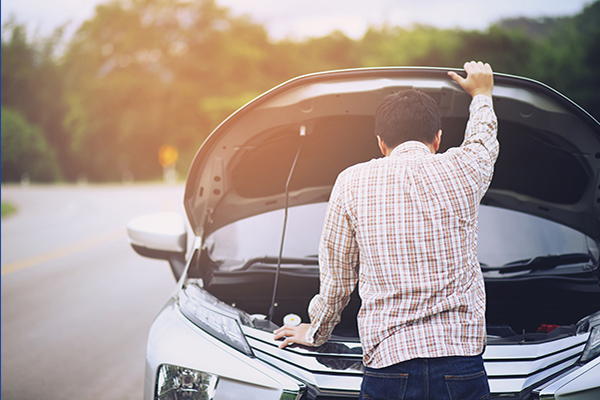A man has the hood of his car open and is looking at the engine inside.