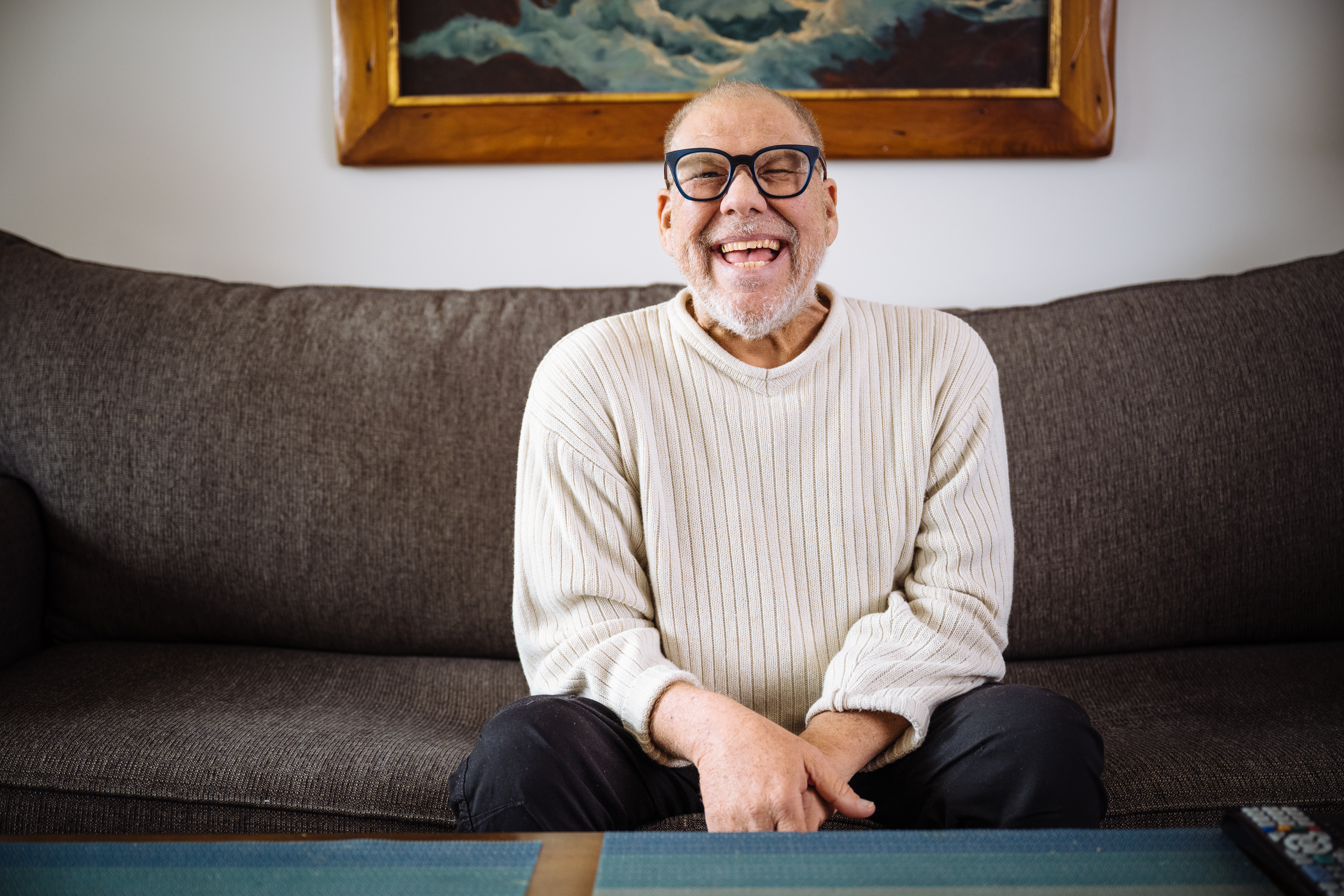 Individual smiling on couch and happily living in supportive housing.